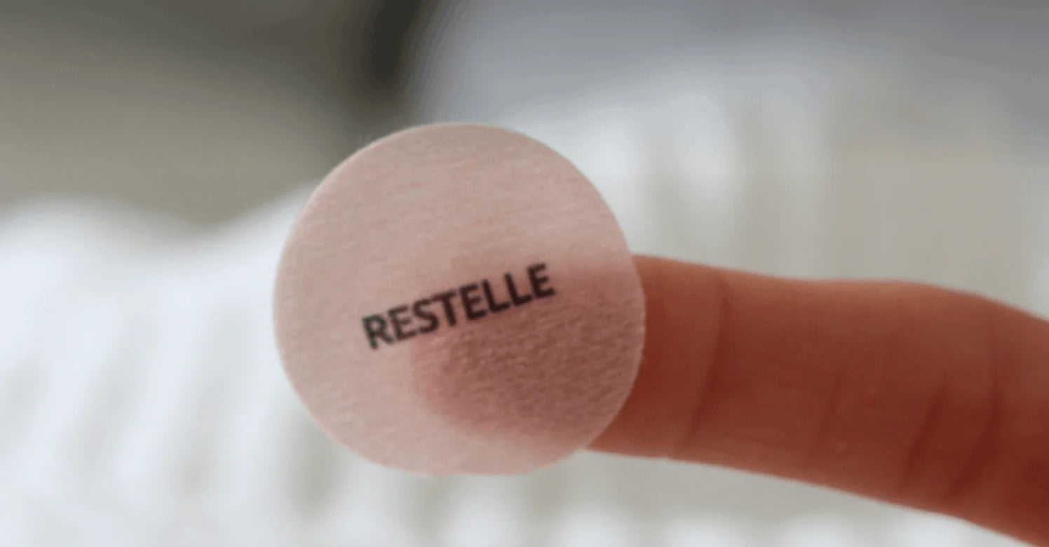 A close-up of a fingertip holding a small, round, translucent patch with the word ELANESSA on it.